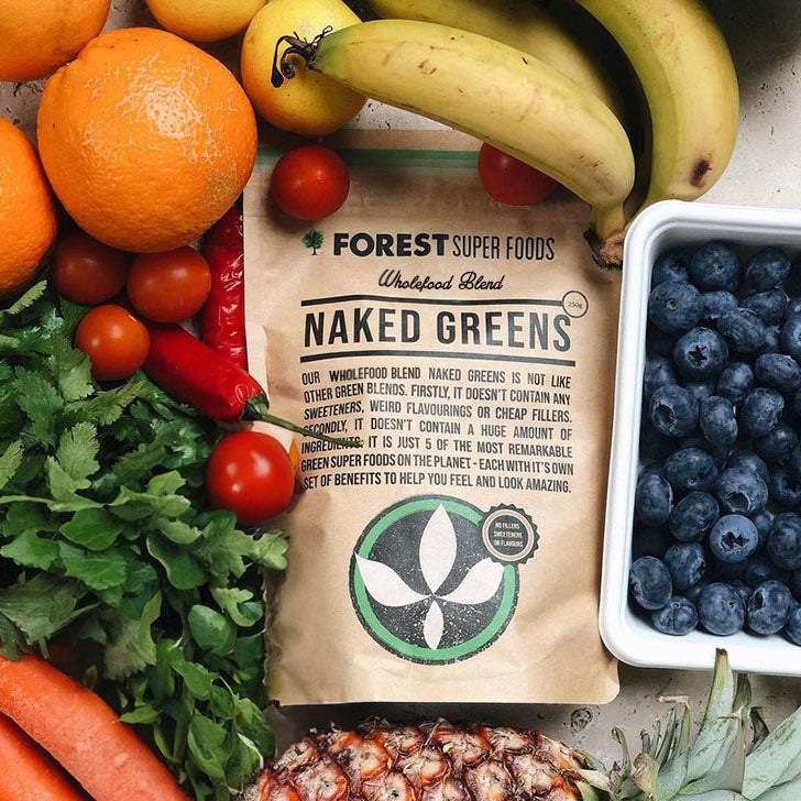 Naked Greens Capsules pouch from Forest Super Foods surrounded by fresh fruits and leafy greens illustrating whole food nutrition